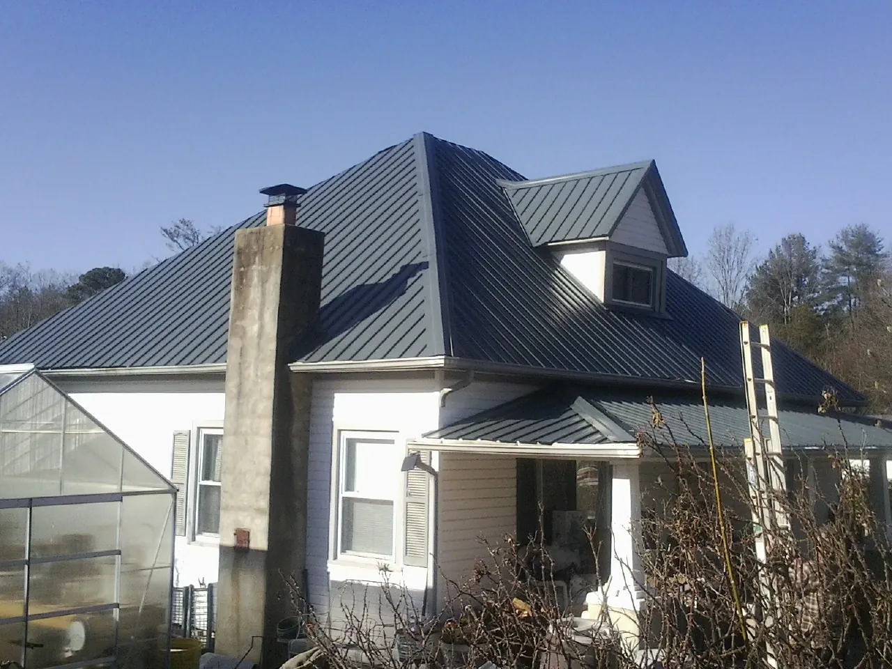 Dark blue standing seam metal roof on a white farmhouse with dormer — Slate & Tile Roof Repair by Roofing Brothers in Granite