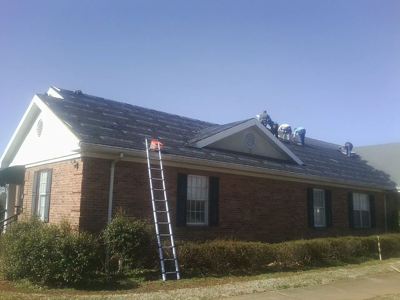 Crew tearing shingles off a brick ranch roof with a ladder set — Emergency Roof Repair work by our crew in Granite