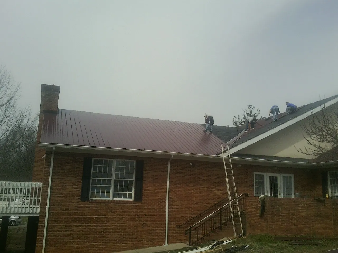 Crew setting red metal roofing panels on a brick home in Granite