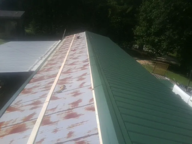 Old rusted panels beside newly installed green metal roofing — Wind Damage Roof Repair by Roofing Brothers in Granite