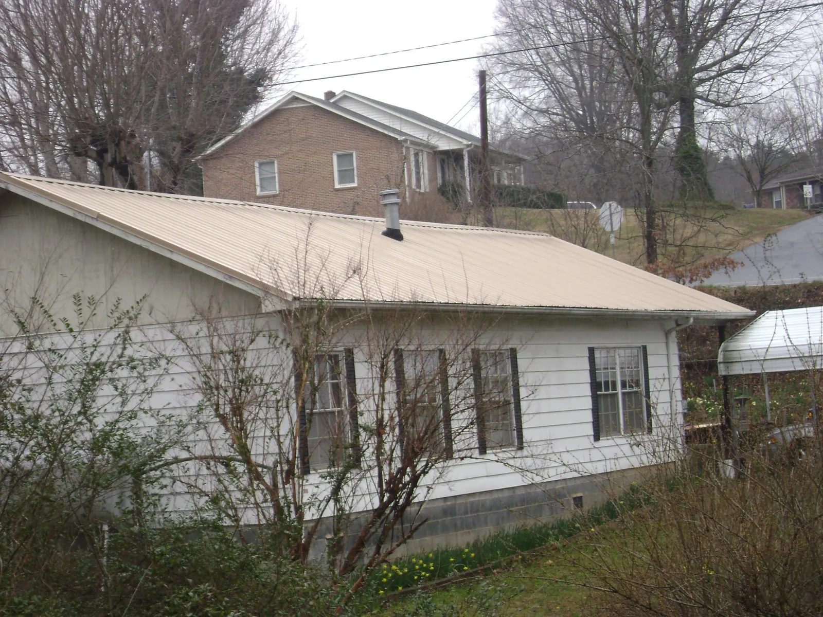 Tan metal roof on a white sided house set into a hillside — Commercial Roofing by Roofing Brothers in Granite